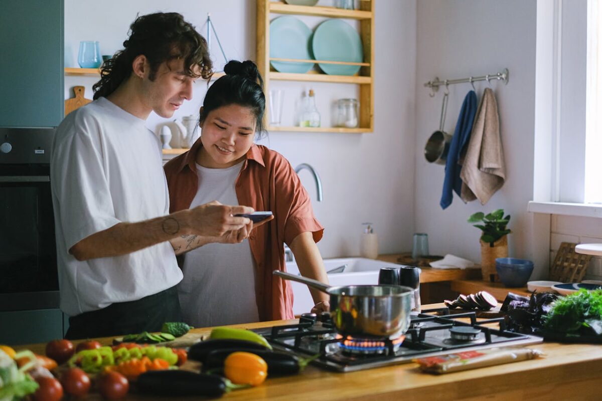 Two people preparing a meal using fresh vegetables and a smartphone for recipe guidance
