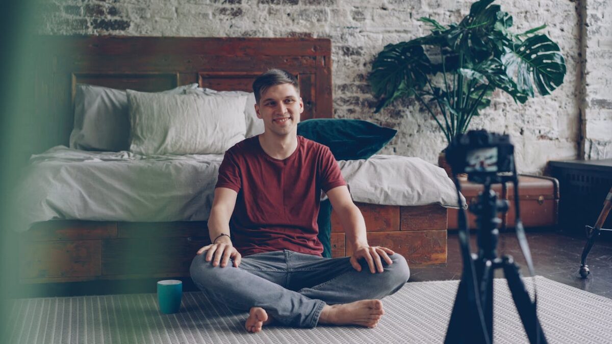 Young adult male vlogger sitting in bedroom, recording content.